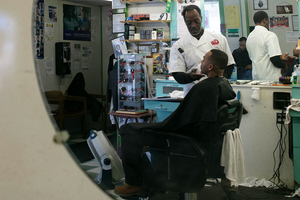 Manager Charleston Collins shaves customer Jameal McMullin last weekend. Underneath the apron, McMullin wore a Collins Barber & Beauty Shop shirt, a nod to his admiration of the South Crouse Avenue shop.