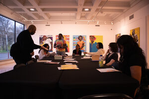 Education Outreach Program Coordinator Cedric T. Bolton passes papers to students participating in the Poetic Black Fusion Workshop. The group met in the Community Folk Art Center's gallery, which features Megan Lewis' Chromatic Expressions paintings.