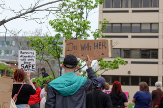 A sign reading “I’m with her” and arrows pointing in all directions shows the protestor’s support for all of the women around them. 
