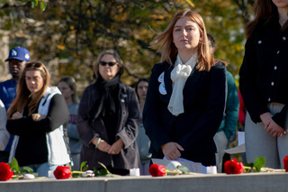 Roses placed in memory of each of the 35 SU abroad student victims line the wall in front of Remembrance Scholar Kinley Gaudette. Gaudette stands solemnly as she waits to be joined by the rest of her cohort. 